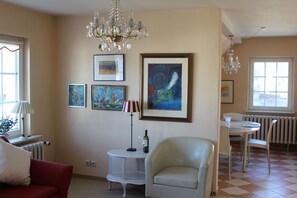 Un salon avec un lustre, une table à manger, des chaises, un canapé rouge et des œuvres d’art accrochées aux murs.