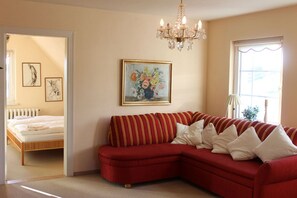 Ein Zimmer mit einem roten Sofa, einer Kristallleuchter, einem Gemälde und einem Fenster mit Blick.