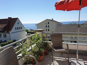 Ein Balkon mit Korbstühlen, Topfpflanzen und einem roten Sonnenschirm.
