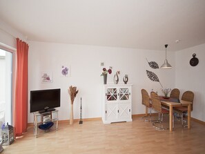 Sala de estar com televisão, armário branco, mesa de jantar, cadeiras e objetos decorativos.
