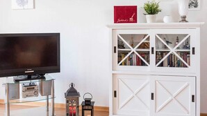 Una sala de estar con un televisor de pantalla plana, un aparador blanco con puertas de cristal y dos faroles decorativos.