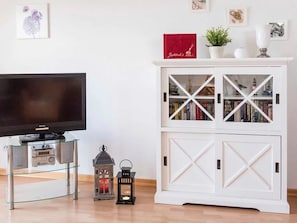 Ein Wohnzimmer mit einem Flachbildfernseher, einem weißen Schrank mit Glastüren und zwei dekorativen Laternen.