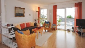 Una sala de estar con sofá, sillas, televisor y vistas al exterior.