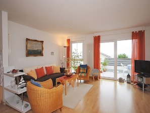 Ein Wohnzimmer mit einer Couch, Sesseln, einem Fernseher und Blick ins Freie.