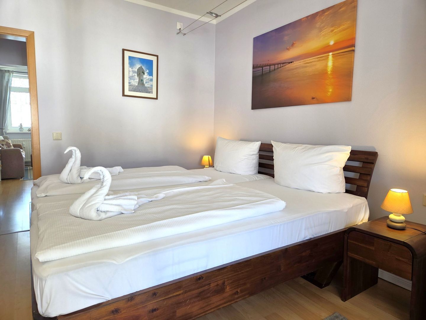 A hotel room with a bed, two bedside lamps, a painting, and a framed picture on the wall.