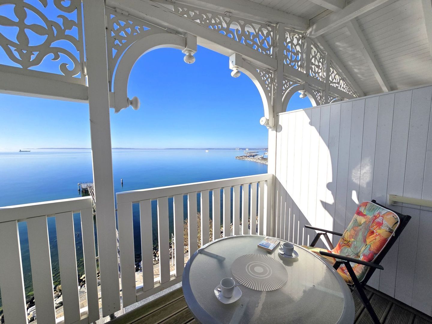 A balcony with a clear view of the sea, a table with a cup and saucer, and a chair.