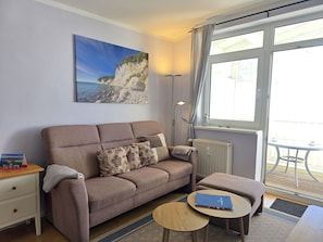 Ein Wohnzimmer mit einer Couch, einem kleinen Tisch, einer Lampe und einem Gemälde einer Küstenlandschaft.