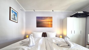 A hotel room with two beds, a painting of a sunset, a wardrobe, and a lamp on the nightstand. - Fürstenhof App. 405 - with balcony and sea view - Fürstennhof, App. 405 - 1. (Sassnitz auf Rügen)