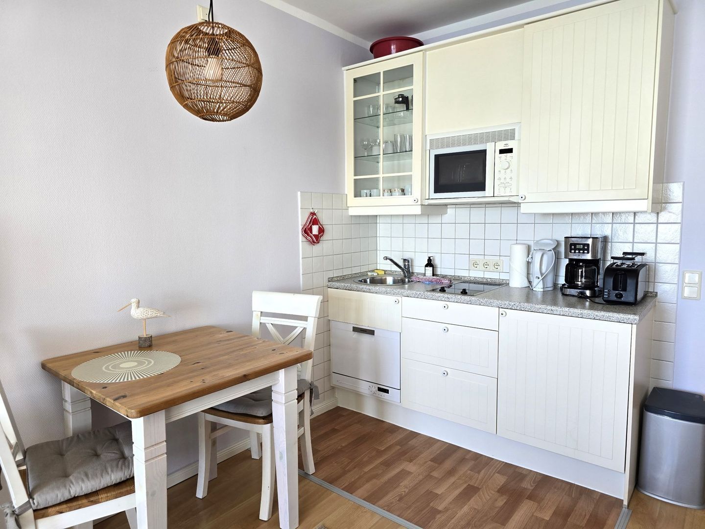 Cuina compacta amb armaris blancs, microones, cafetera i rentatge.