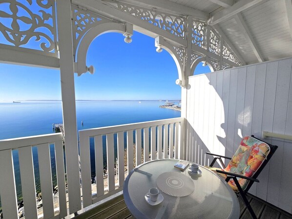 Ein Balkon mit freiem Blick auf das Meer, ein Tisch mit Tasse und Untertasse sowie ein Stuhl.