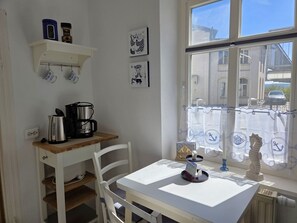 A small kitchen with a coffee maker, a white table, and a window with a view of buildings outside. - Vacation apartment in Haus Amalie - Holiday apartment in Haus Amalie - close to the beach in (Sassnitz auf Rügen)