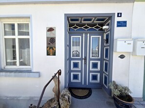 A building entrance with a blue door, a window with a curtain, a wall-mounted sign, and a potted plant. - Vacation apartment in Haus Amalie - Holiday apartment in Haus Amalie - close to the beach in (Sassnitz auf Rügen)