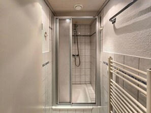 A narrow, enclosed shower area with a glass door, a handheld showerhead, and a bathtub. - Vacation apartment in Haus Amalie - Holiday apartment in Haus Amalie - close to the beach in (Sassnitz auf Rügen)