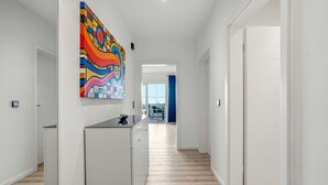 Un couloir moderne avec un coin cuisine, une peinture abstraite aux couleurs vives et une vue sur un balcon.