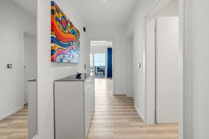 Ein moderner Flur mit Küchenbereich, einem farbenfrohen abstrakten Gemälde und Blick auf einen Balkon.
