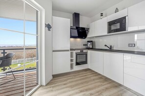 Eine moderne Küche mit Einbauofen, Mikrowelle und Kaffeemaschine, eine Glastür zum Balkon und ein Holzboden.