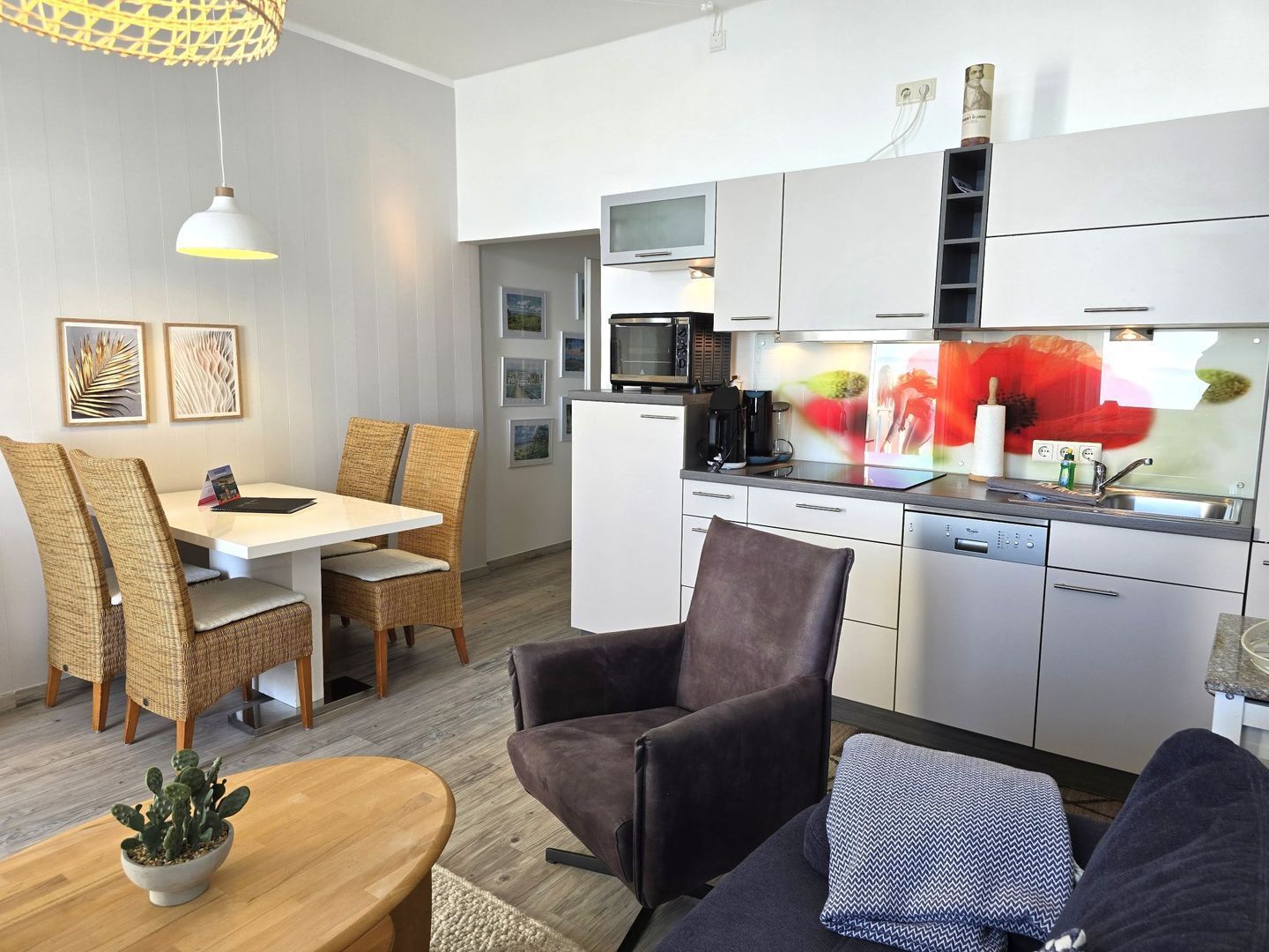 Une cuisine moderne avec des meubles blancs, un four à micro-ondes et une machine à café. On y trouve également un coin repas avec des chaises et une table en osier.