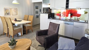 Una cucina moderna con mobili bianchi, un forno a microonde e una macchina da caffè. C'è un'area pranzo con sedie in vimini e un tavolo.