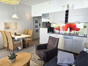 A modern kitchen with white cabinets, a microwave, and a coffee maker. There is a dining area with wicker chairs and a table. - Fürstenhof, App. 304 - First row by the sea - Fürstenhof, App. 304 - Front row, (Sassnitz auf Rügen)