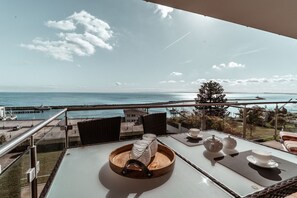 A balcony with a table set for tea, overlooking a coastal view with a pier and a clear sky. - Villa Friede-Marie, App. Freya - with wonderful sea view - Villa Friede-Marie, (Sassnitz auf Rügen)