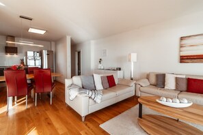 A modern living room with a sofa, a dining table with chairs, and a kitchen in the background. - Villa Friede-Marie, App. Freya - with wonderful sea view - Villa Friede-Marie, (Sassnitz auf Rügen)