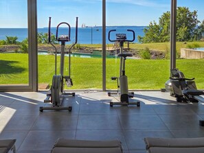 Ein Fitnessraum mit Trainingsgeräten und Blick auf das Meer.