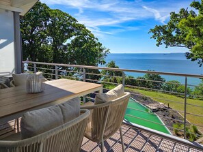 Ein Balkon mit Tisch und Stühlen, der auf einen grünen Pool und Meerblick blickt.
