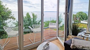 Una habitación moderna con ventanas amplias, una terraza de madera y sillas de mimbre blanco.
