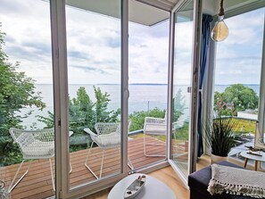 Ein modernes Zimmer mit großen Fenstern, einer Holzdielen-Terrasse und weißen Korbstühlen.