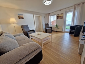 Ein modernes Wohnzimmer mit einer Couch, Sesseln, einem Couchtisch und einem Fernseher.