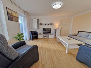 Ein modernes Wohnzimmer mit einer Couch, einem Couchtisch, einem Fernseher und einer kleinen Kommode.
