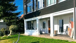 Ett modernt hus i två våningar med en täckt uteplats, en gräsmatta och en stol.