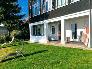 Ein modernes, zweistöckiges Haus mit überdachter Terrasse, Rasen und einem Stuhl.