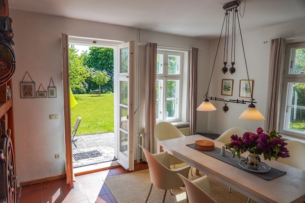 Eine offene Tür, die in einen Garten führt, ein Esstisch mit Stühlen und eine hängende Leuchte.