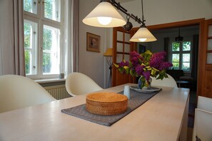 Ein Essbereich mit Tisch, Stühlen, Blumen in einer Vase und einem Fenster mit Vorhängen.
