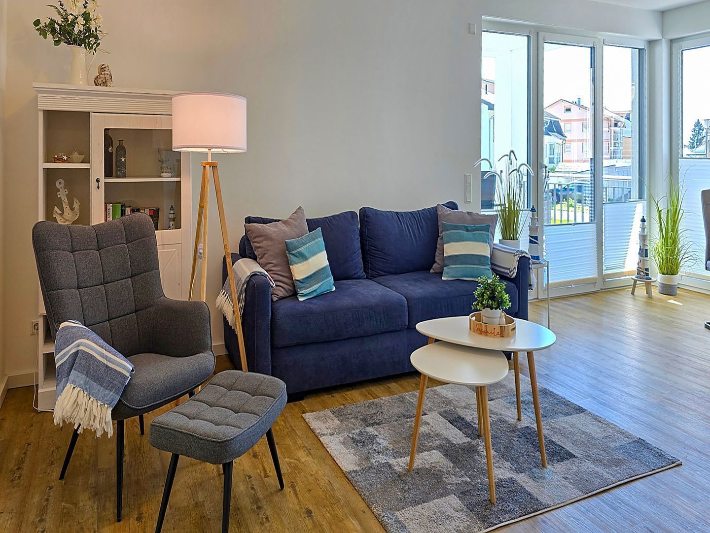 Un salon comprenant un canapé, un fauteuil et un pouf, une lampe sur pied et une petite table sur laquelle est posée une plante.