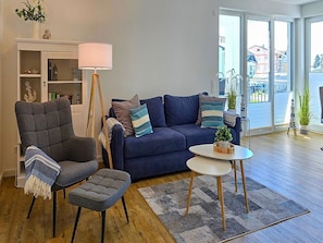 Ein Wohnzimmer mit Sofa, Sesseln, einem Hocker, einer Stehlampe und einem kleinen Tisch mit einer Pflanze.