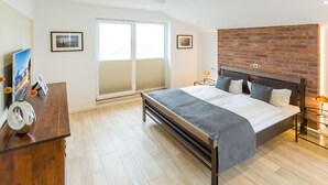 A bedroom with a bed, a dresser, a TV, and a brick wall. - Villa am Kreidebruch, FeWo OstseeWeitblick - panoramic view of the Baltic Sea (Sassnitz auf Rügen)