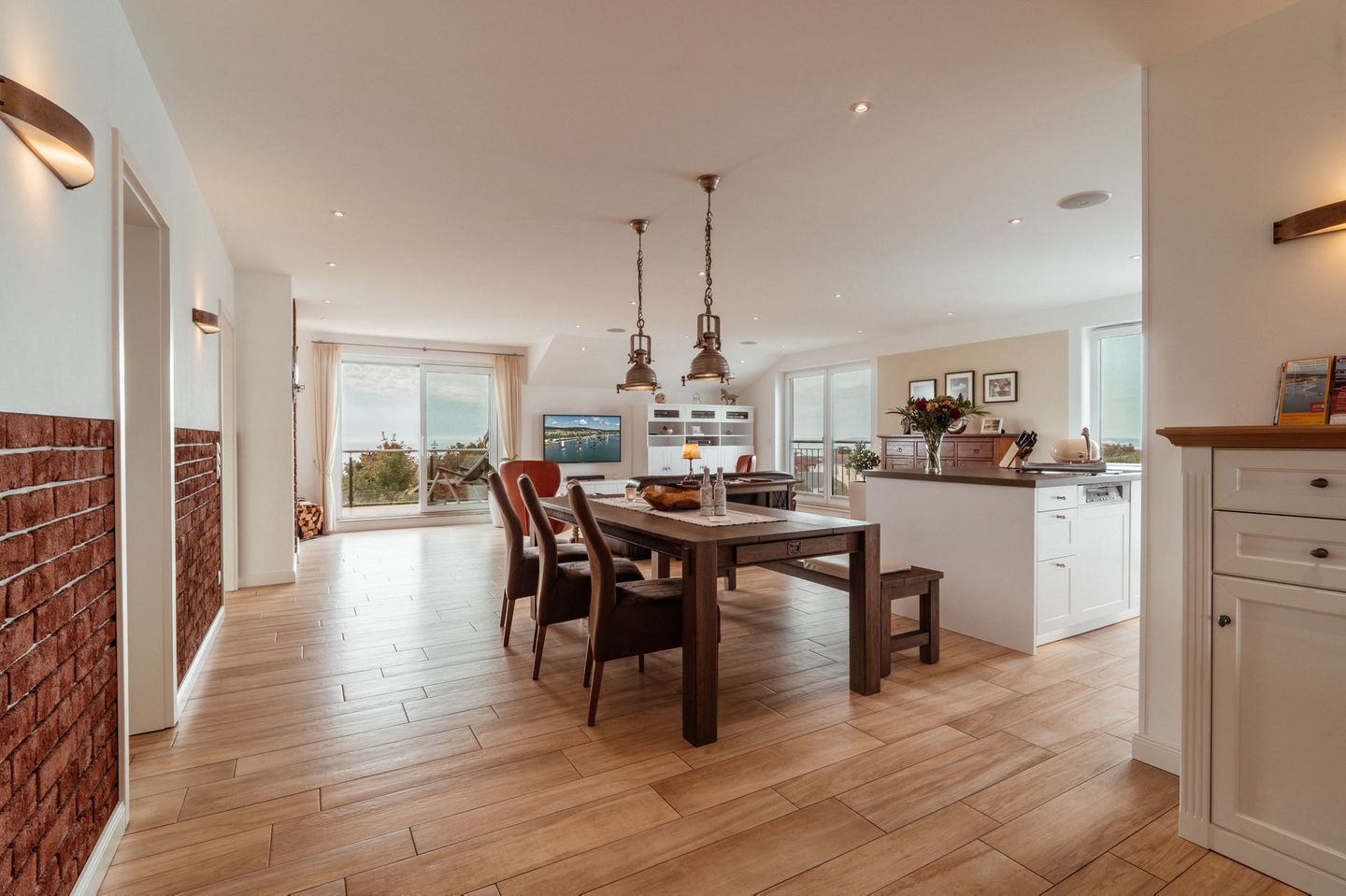 A modern kitchen with a dining area, wooden flooring, and a view to the outside.