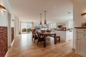 A modern kitchen with a dining area, wooden flooring, and a view to the outside. - Villa am Kreidebruch, FeWo OstseeWeitblick - panoramic view of the Baltic Sea (Sassnitz auf Rügen)