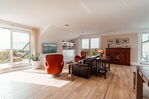 Un salon spacieux avec une grande fenêtre, un fauteuil rouge, un canapé noir et une table basse en bois.