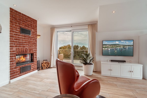 A living room with a fireplace, a television, a potted plant, and a view of the outdoors. - Villa am Kreidebruch, FeWo OstseeWeitblick - panoramic view of the Baltic Sea (Sassnitz auf Rügen)