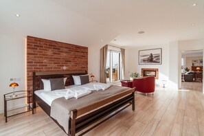 A modern bedroom with a brick accent wall, a large bed, a red armchair, and a view of the city. - Villa am Kreidebruch, FeWo OstseeWeitblick - panoramic view of the Baltic Sea (Sassnitz auf Rügen)