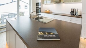 A modern kitchen with a large island, stainless steel appliances, and a view of the outside. - Villa am Kreidebruch, FeWo OstseeWeitblick - panoramic view of the Baltic Sea (Sassnitz auf Rügen)