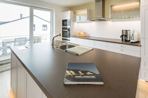 A modern kitchen with a large island, stainless steel appliances, and a view of the outside. - Villa am Kreidebruch, FeWo OstseeWeitblick - panoramic view of the Baltic Sea (Sassnitz auf Rügen)