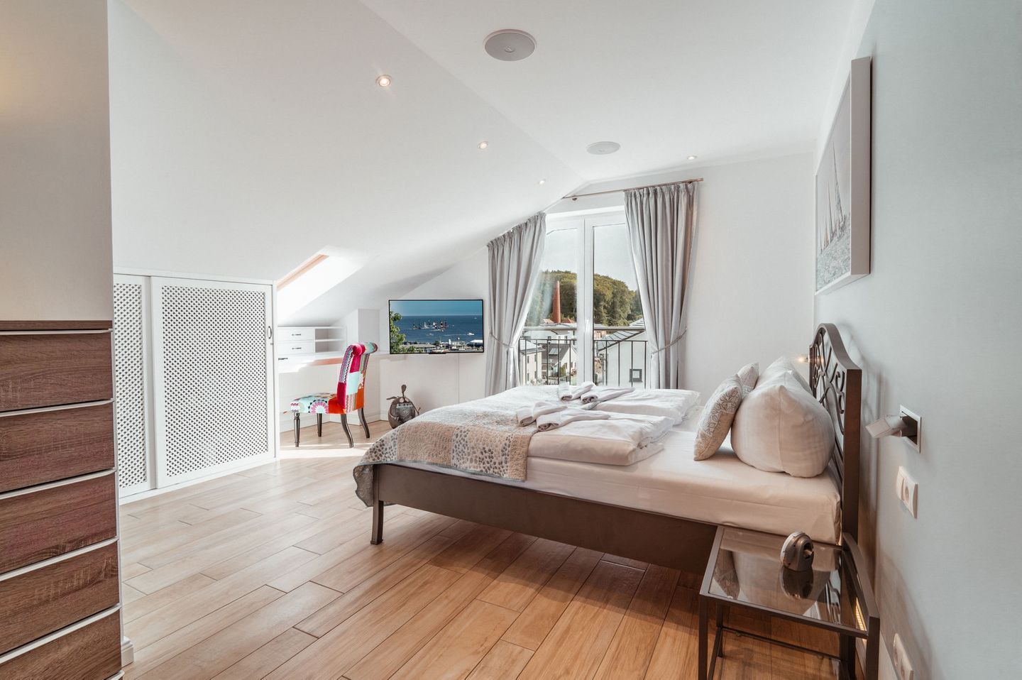 A modern bedroom with a large bed, a desk, and a view of the sea.