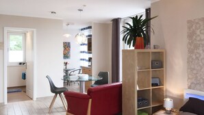 A modern living room with a glass dining table, red sofa, and a bookshelf. - Apartment Richi - central and quiet in the harbor town of Sassnitz - (Sassnitz auf Rügen)