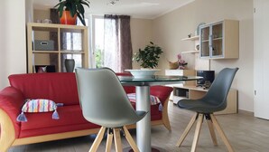 A modern living room with a red sofa, two grey chairs, a glass-top coffee table, and a television. - Apartment Richi - central and quiet in the harbor town of Sassnitz - (Sassnitz auf Rügen)