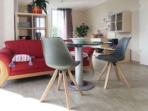Ein modernes Wohnzimmer mit einem roten Sofa, zwei grauen Sesseln, einem Couchtisch aus Glas und einem Fernseher.