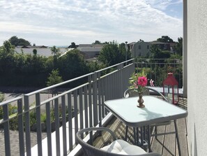 Ein Balkon mit Tisch und Stühlen, einem Geländer und Blick auf das Meer und Gebäude.